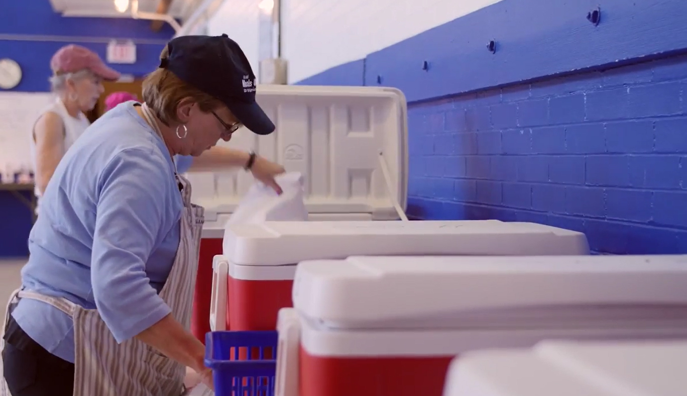 A woman in a hat and apron is putting ice chests together.